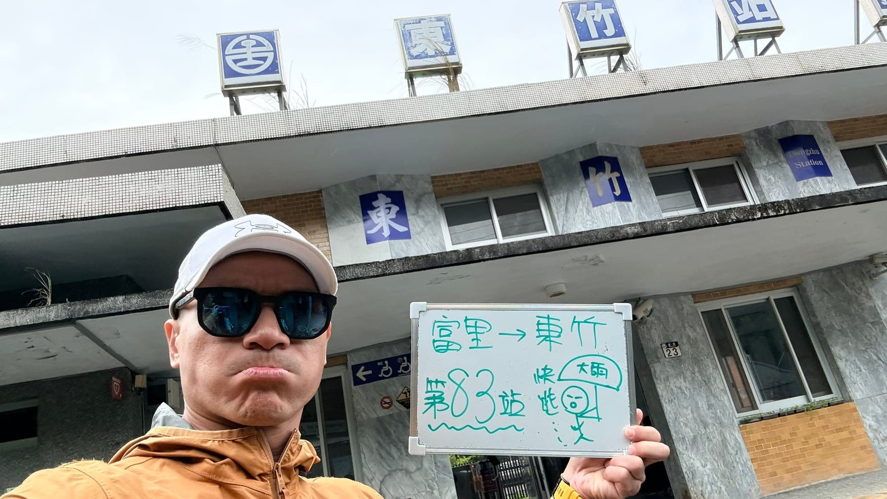 站主在東竹站站牌前的走訪紀錄照，手持寫著「徒步環島 第 83 站　富里 → 東竹」的白板