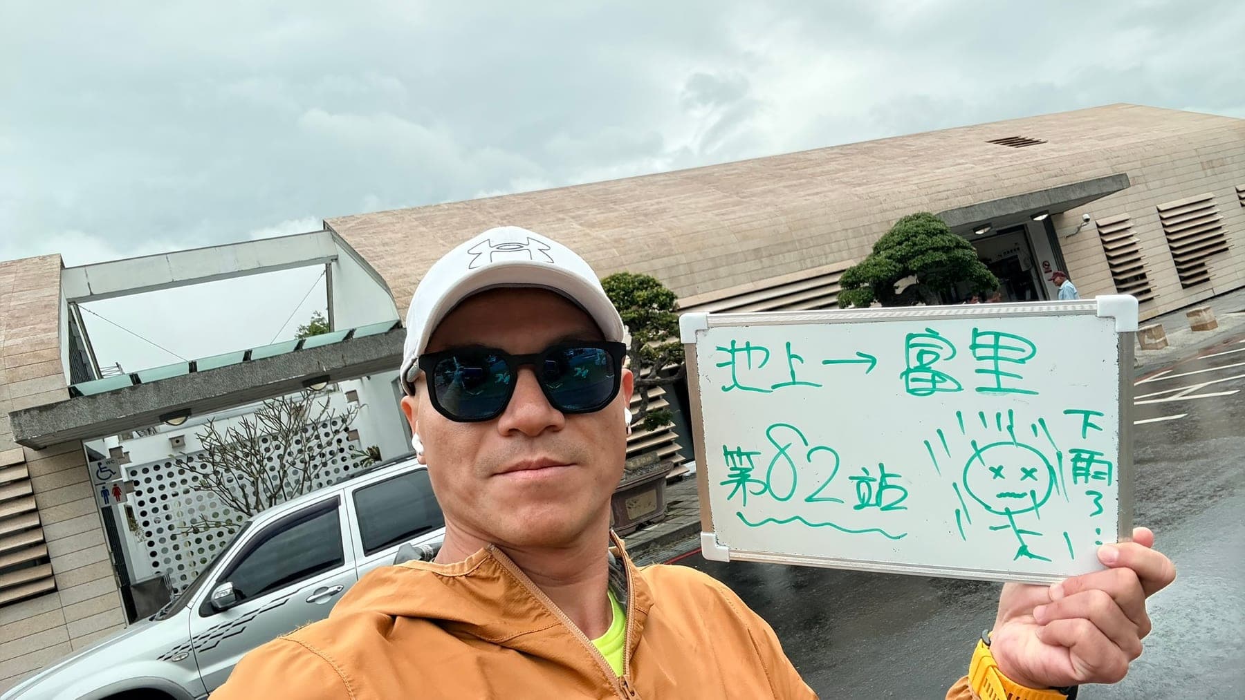 站主在富里站站牌前的走訪紀錄照，手持寫著「徒步環島 第 82 站　池上 → 富里」的白板