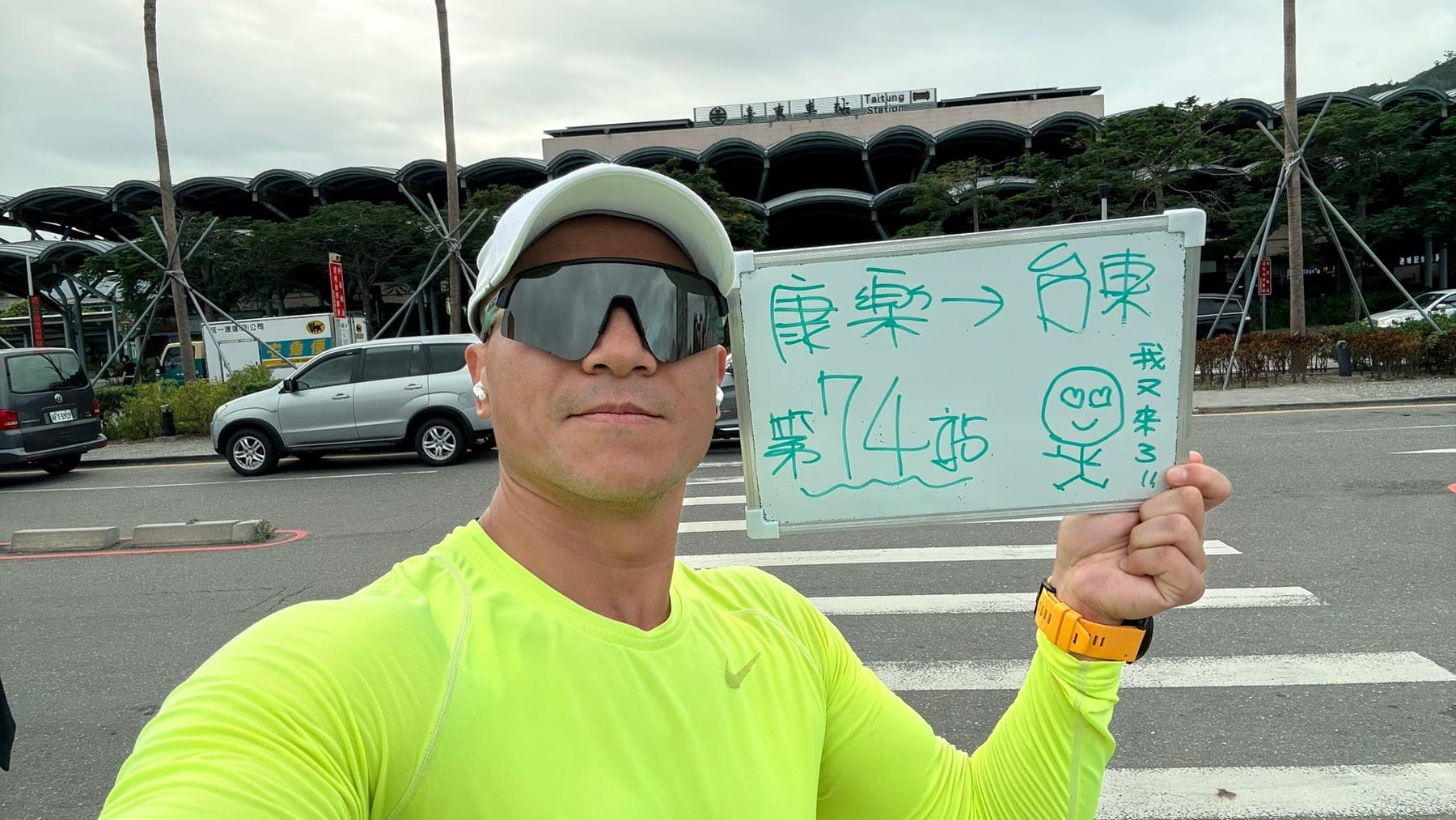 站主在台東站站牌前的走訪紀錄照，手持寫著「徒步環島 第 74 站　康樂 → 台東」的白板