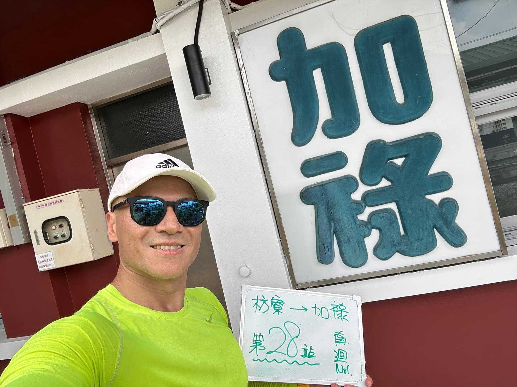 站主在加祿站站牌前的走訪紀錄照，手持寫著「徒步環島 第 28 站　枋寮 → 加祿」的白板