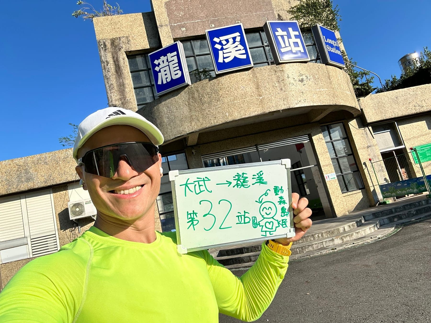 站主在瀧溪站站牌前的走訪紀錄照，手持寫著「徒步環島 第 32 站　大武 → 瀧溪」的白板