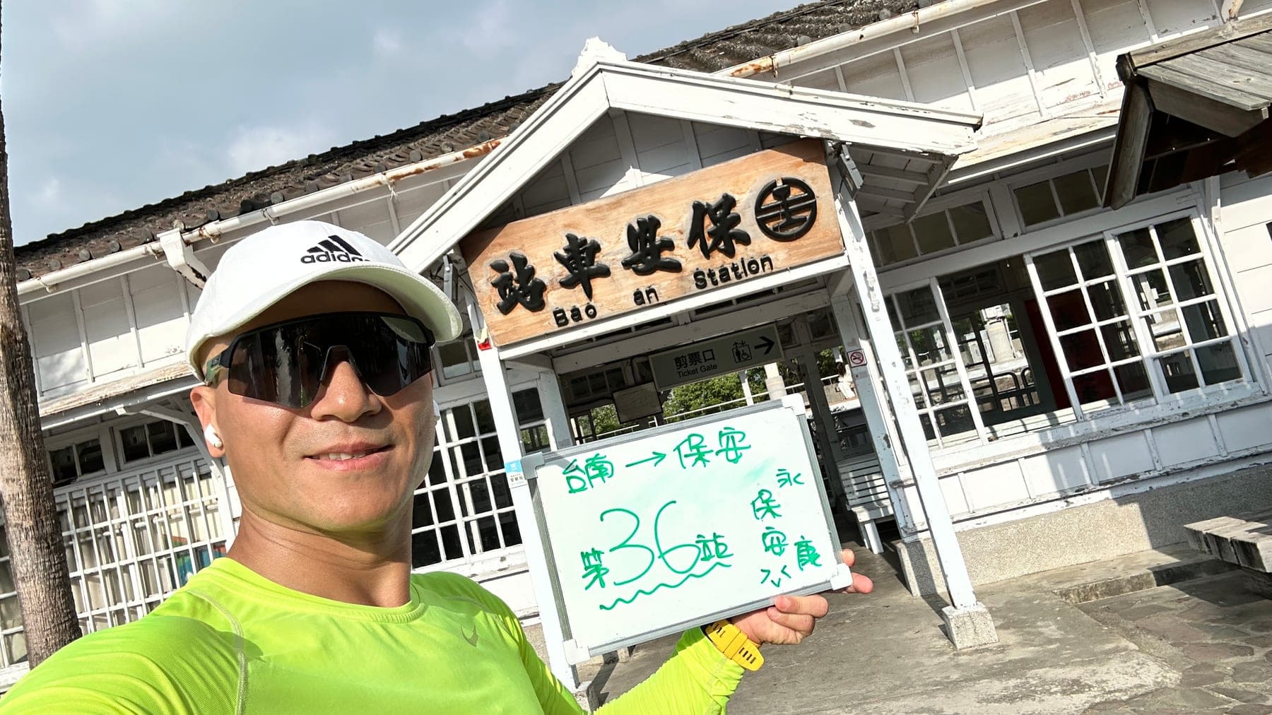 站主在保安站站牌前的走訪紀錄照，手持寫著「徒步環島 第 36 站　台南 → 保安」的白板