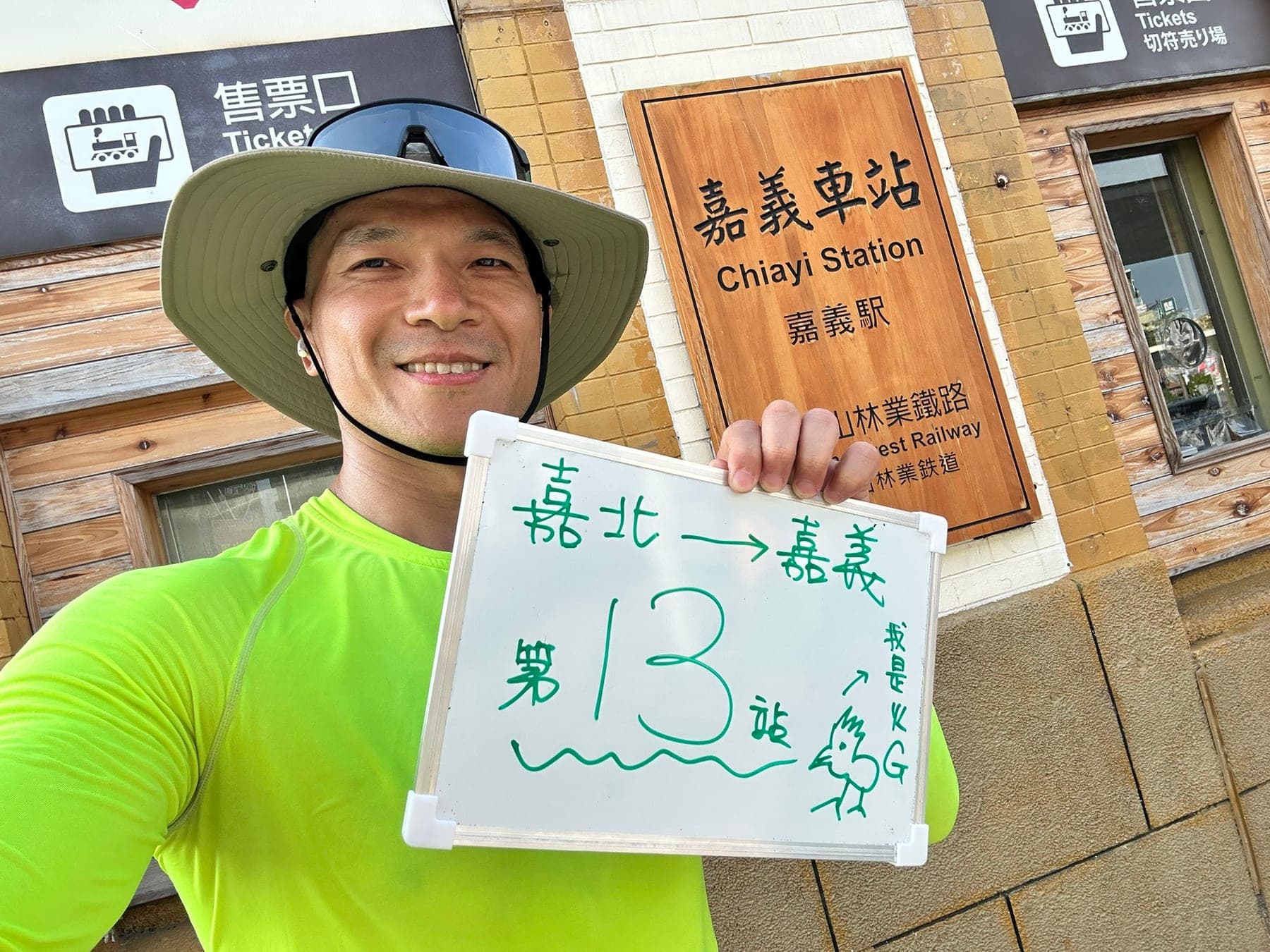 站主在嘉義站站牌前的走訪紀錄照，手持寫著「徒步環島 第 13 站　嘉北 → 嘉義」的白板