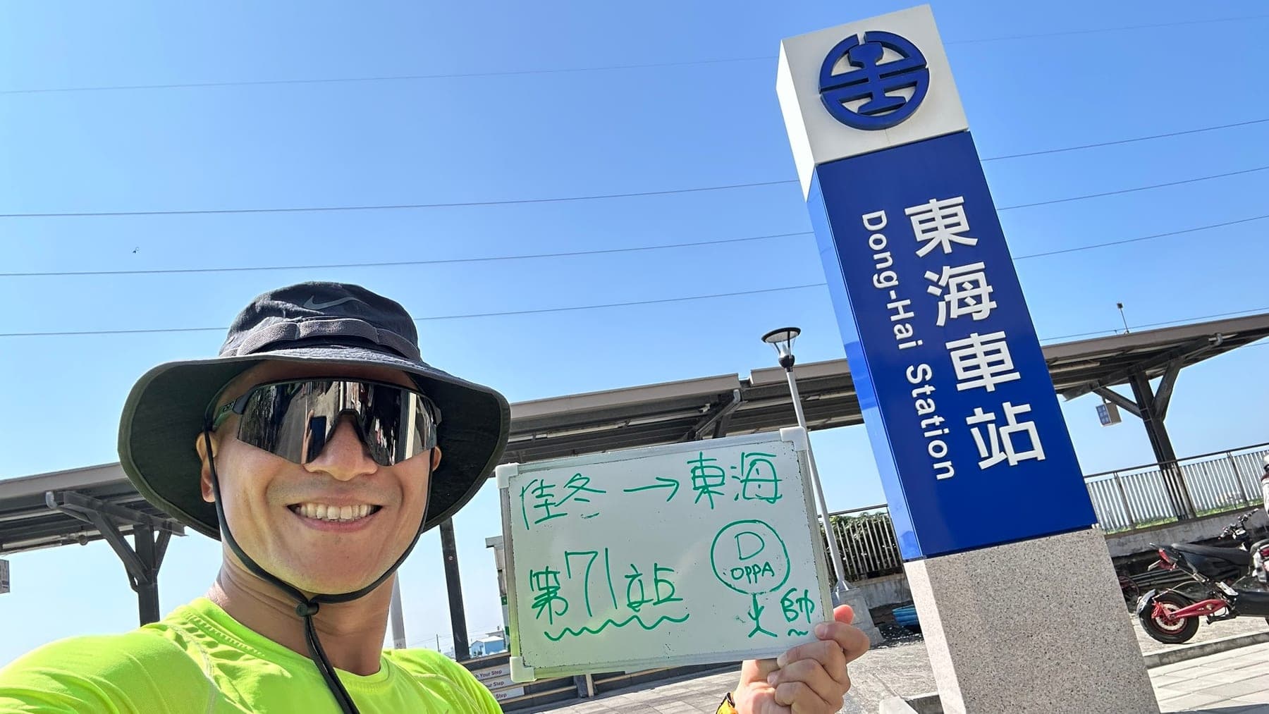 站主在東海站站牌前的走訪紀錄照，手持寫著「徒步環島 第 71 站　佳冬 → 東海」的白板