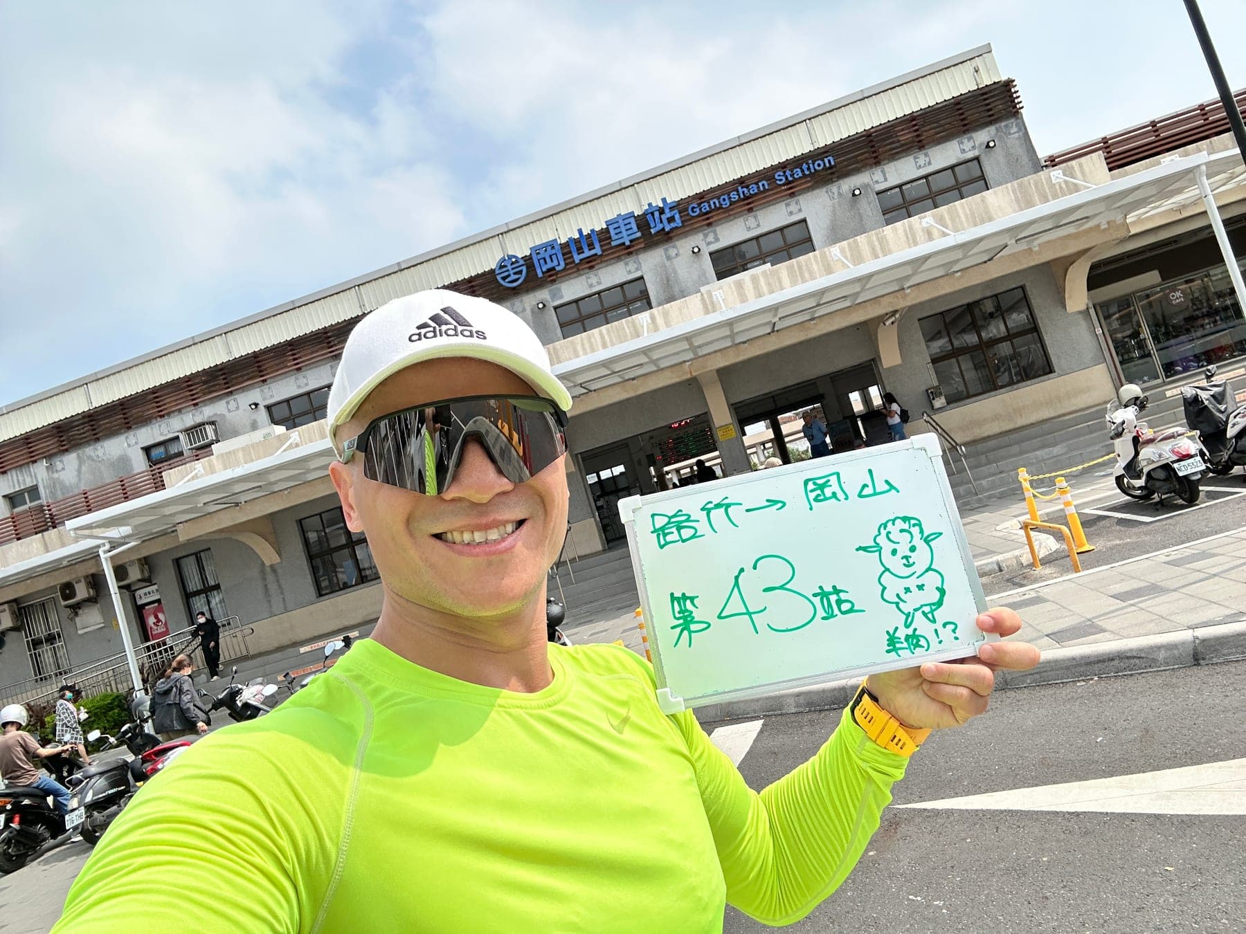 站主在岡山站站牌前的走訪紀錄照，手持寫著「徒步環島 第 43 站　路竹 → 岡山」的白板