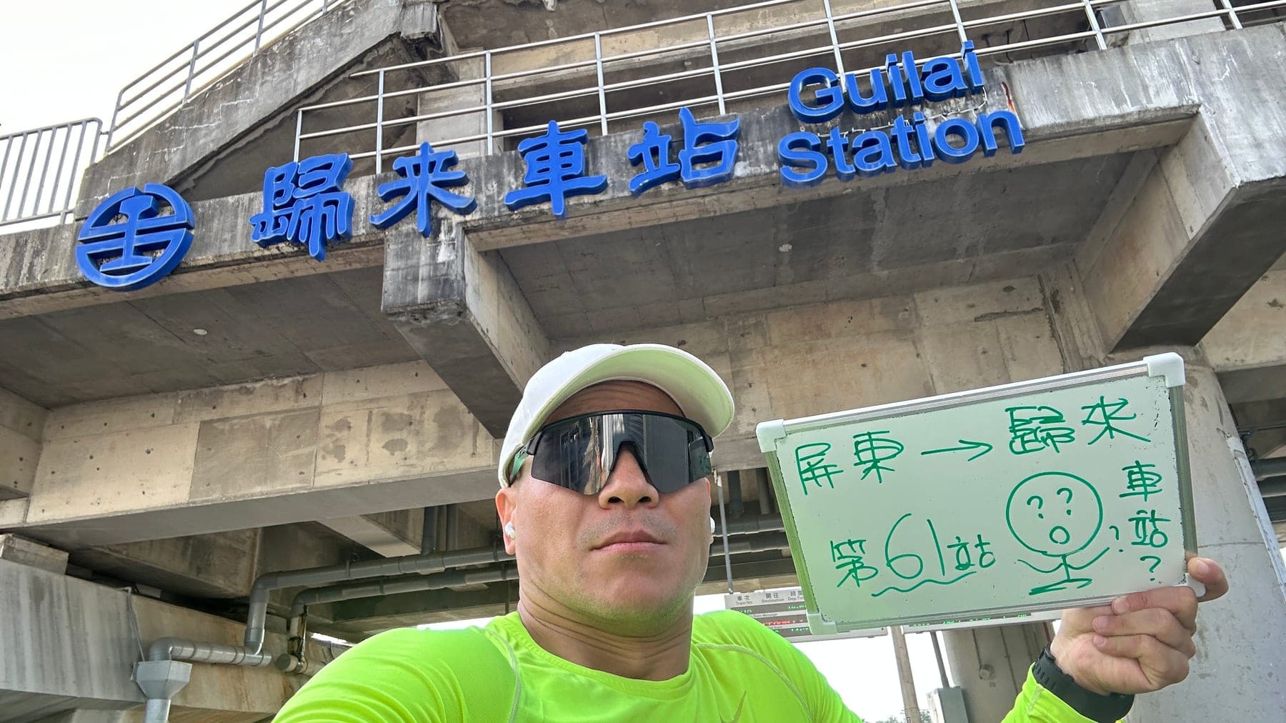 站主在歸來站站牌前的走訪紀錄照，手持寫著「徒步環島 第 61 站　屏東 → 歸來」的白板