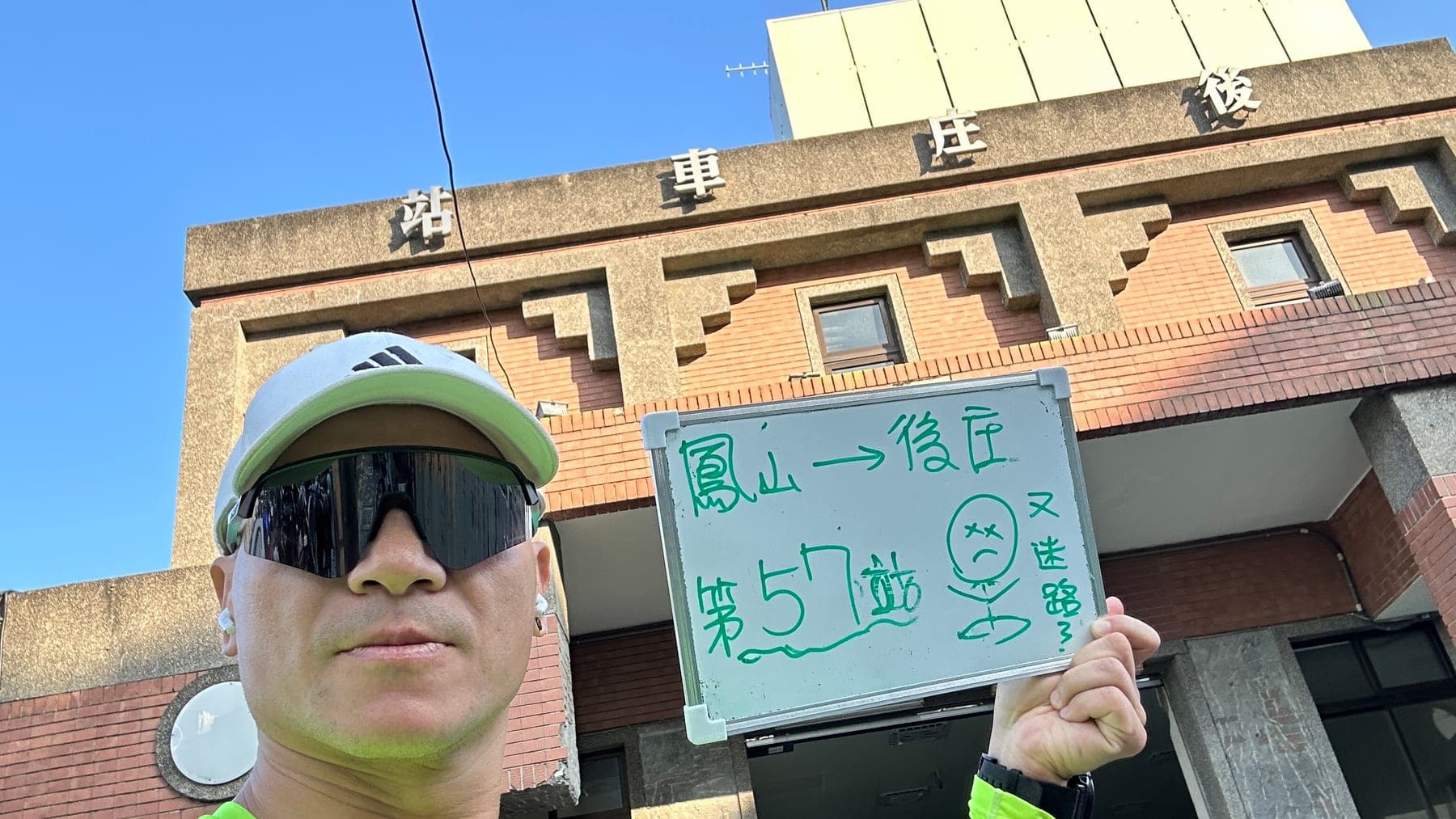 站主在後庄站站牌前的走訪紀錄照，手持寫著「徒步環島 第 57 站　鳳山 → 後庄」的白板