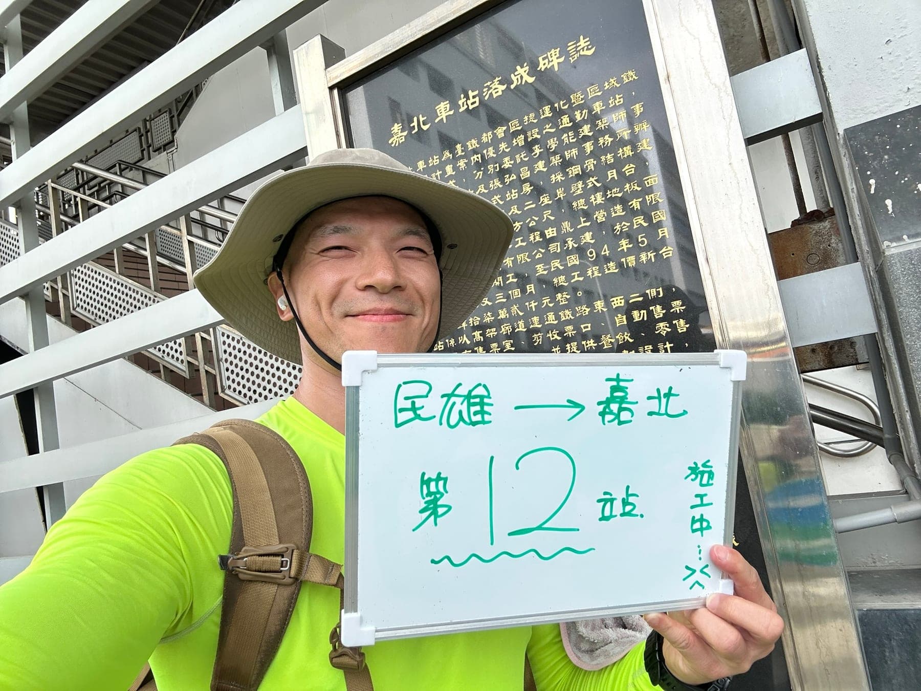 站主在嘉北站站牌前的走訪紀錄照，手持寫著「徒步環島 第 12 站　民雄 → 嘉北」的白板