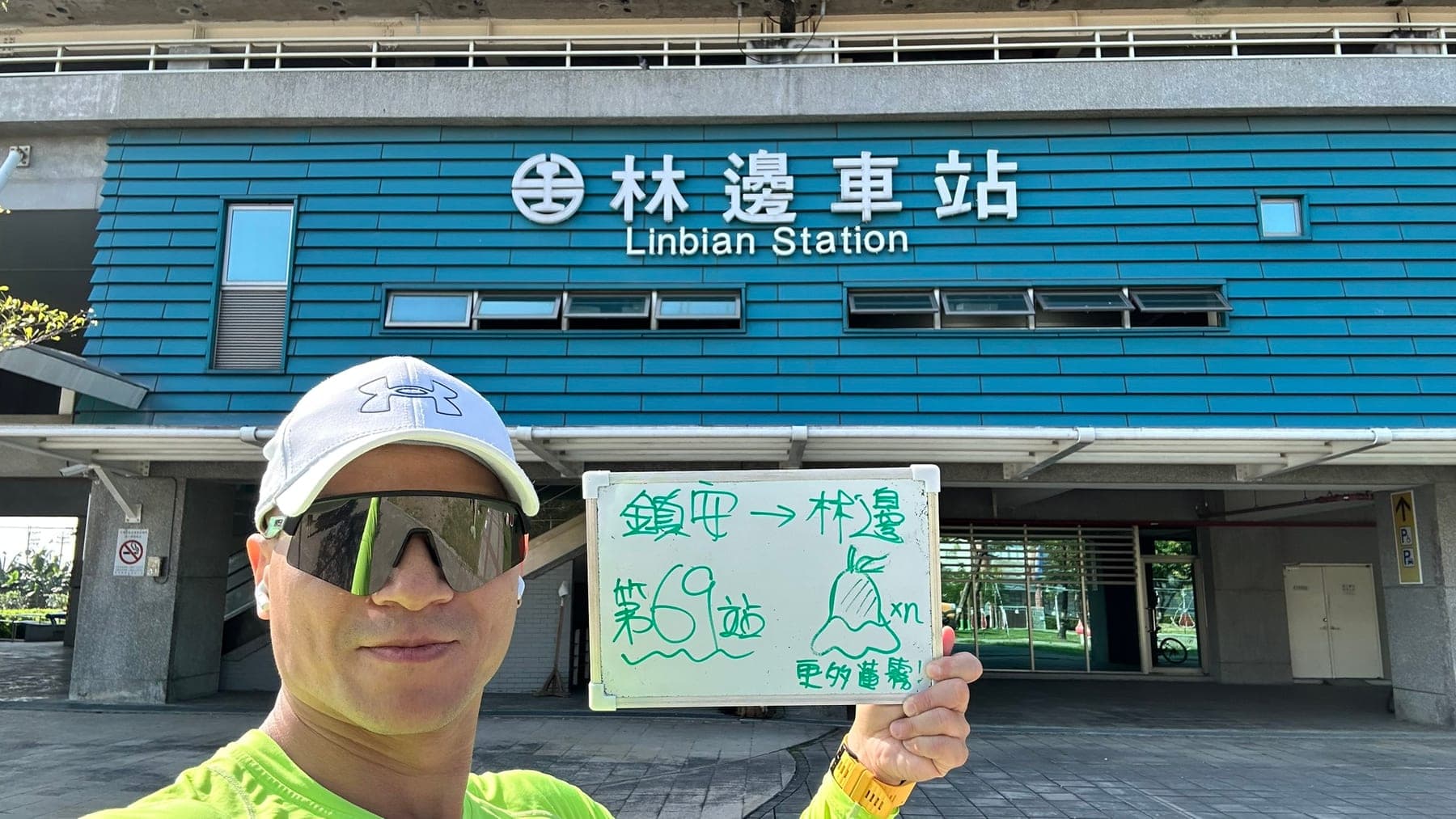站主在林邊站站牌前的走訪紀錄照，手持寫著「徒步環島 第 69 站　鎮安 → 林邊」的白板