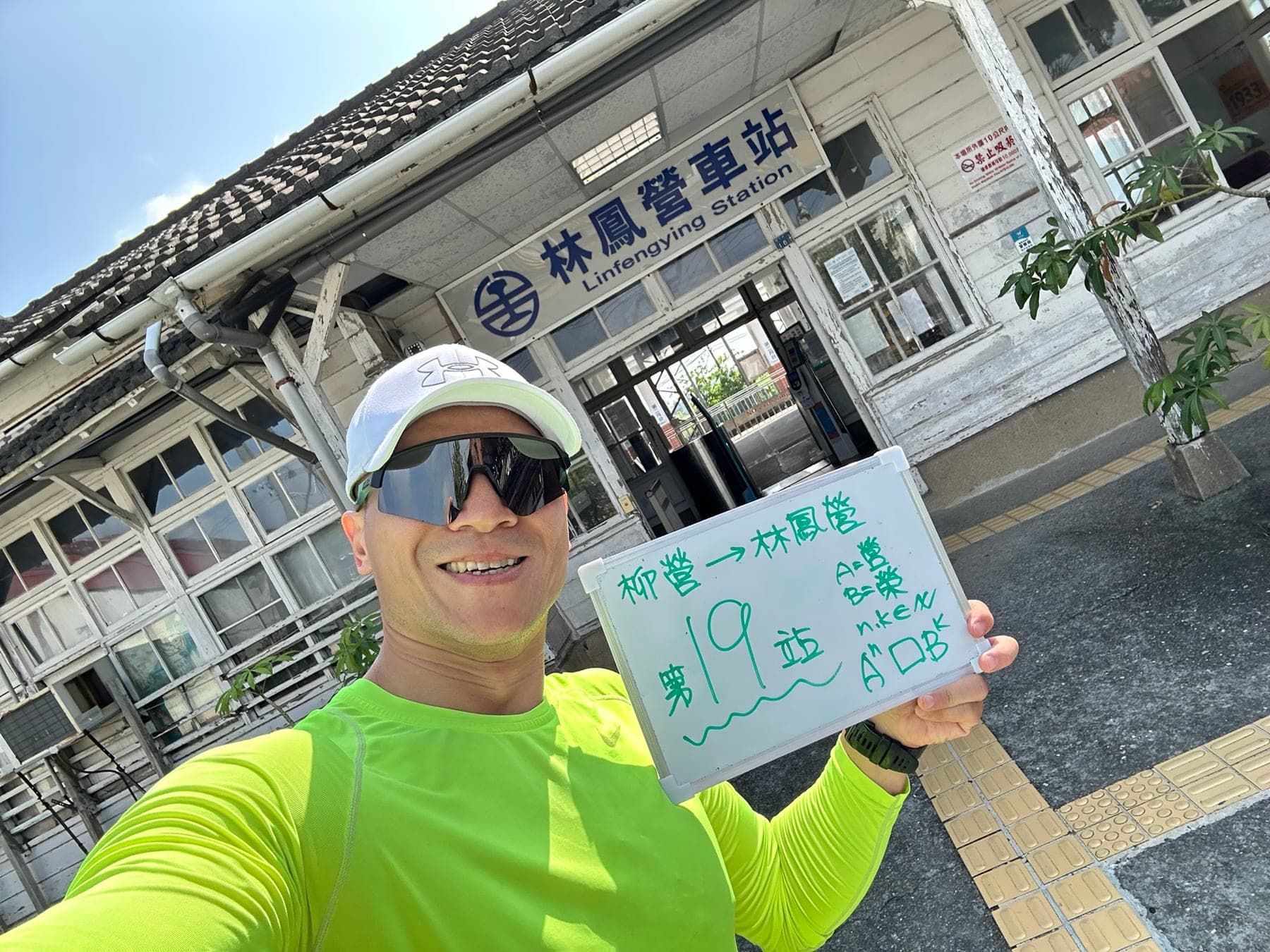 站主在林鳳營站站牌前的走訪紀錄照，手持寫著「徒步環島 第 19 站　柳營 → 林鳳營」的白板
