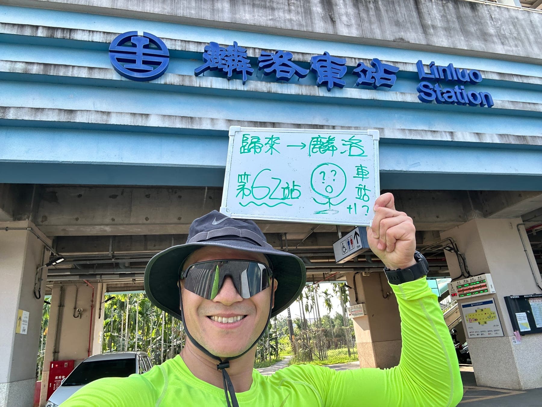 站主在麟洛站站牌前的走訪紀錄照，手持寫著「徒步環島 第 62 站　歸來 → 麟洛」的白板