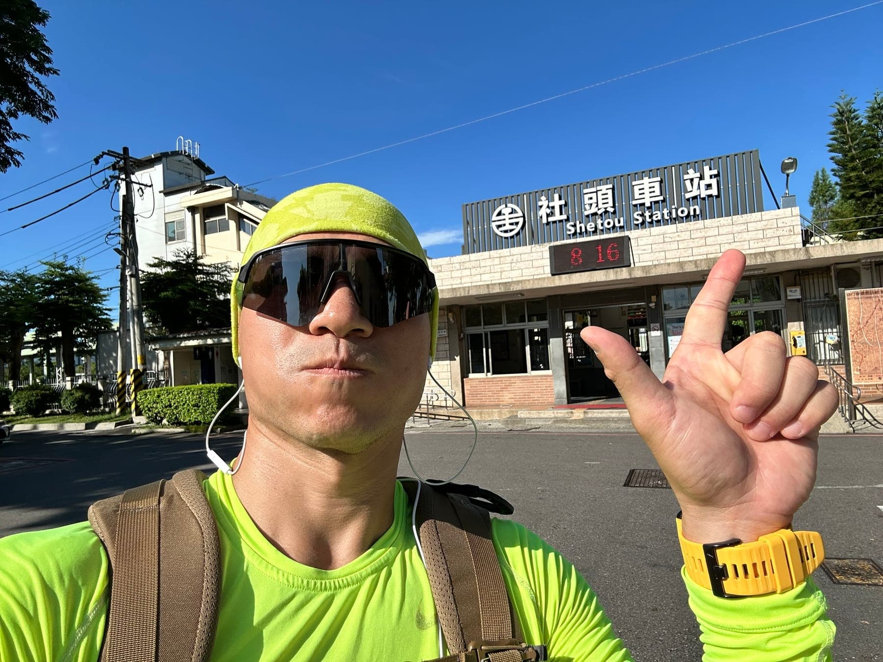 站主在社頭車站前的走訪紀錄照，手比二代表第 2 站，站房上方電子鐘顯示 8:16