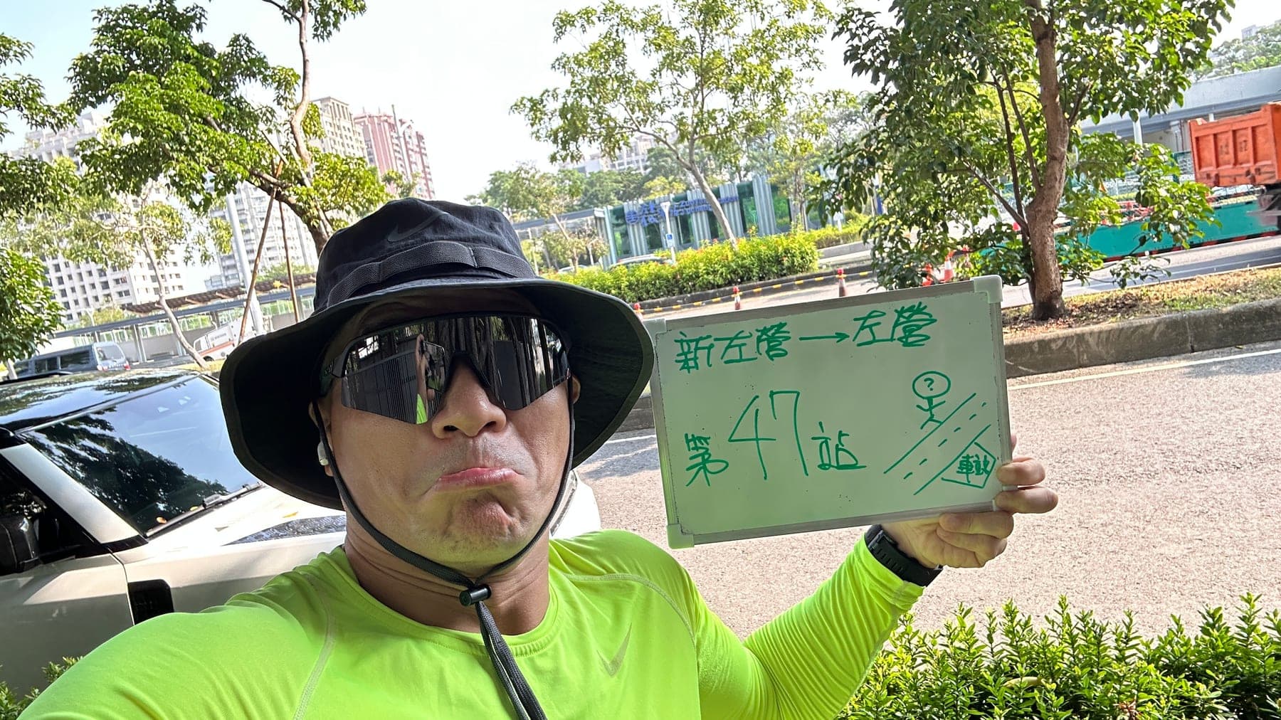 站主在左營(舊城)站站牌前的走訪紀錄照，手持寫著「徒步環島 第 47 站　新左營 → 左營」的白板