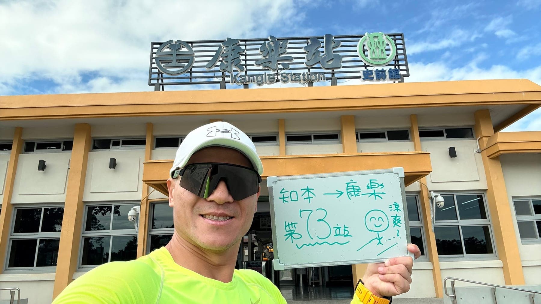 站主在康樂站站牌前的走訪紀錄照,手持寫著「徒步環島 第 73 站 知本 → 康樂」的白板