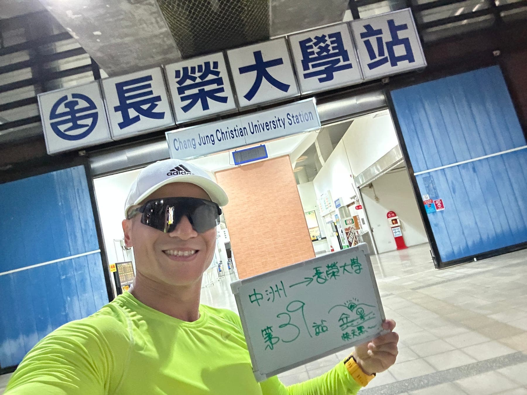 站主在長榮大學站站牌前的走訪紀錄照,手持寫著「徒步環島 第 39 站 中洲 → 長榮大學」的白板