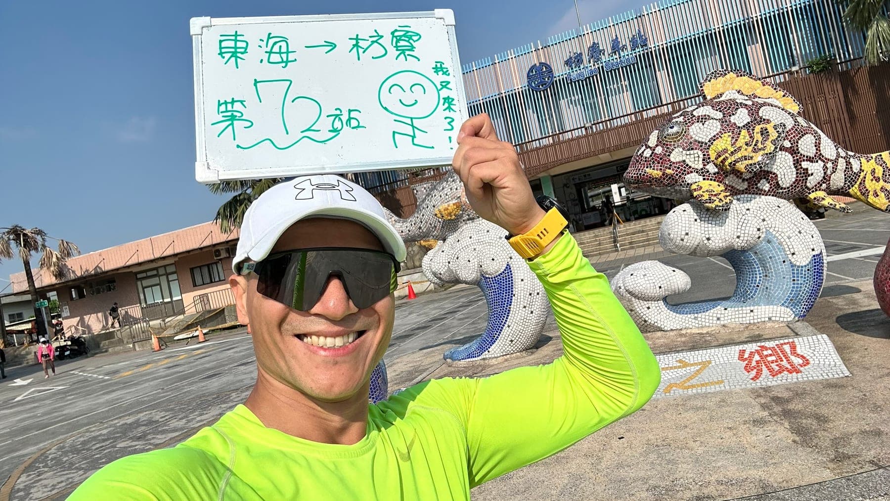 站主在枋寮站站牌前的走訪紀錄照,手持寫著「徒步環島 第 72 站 東海 → 枋寮」的白板