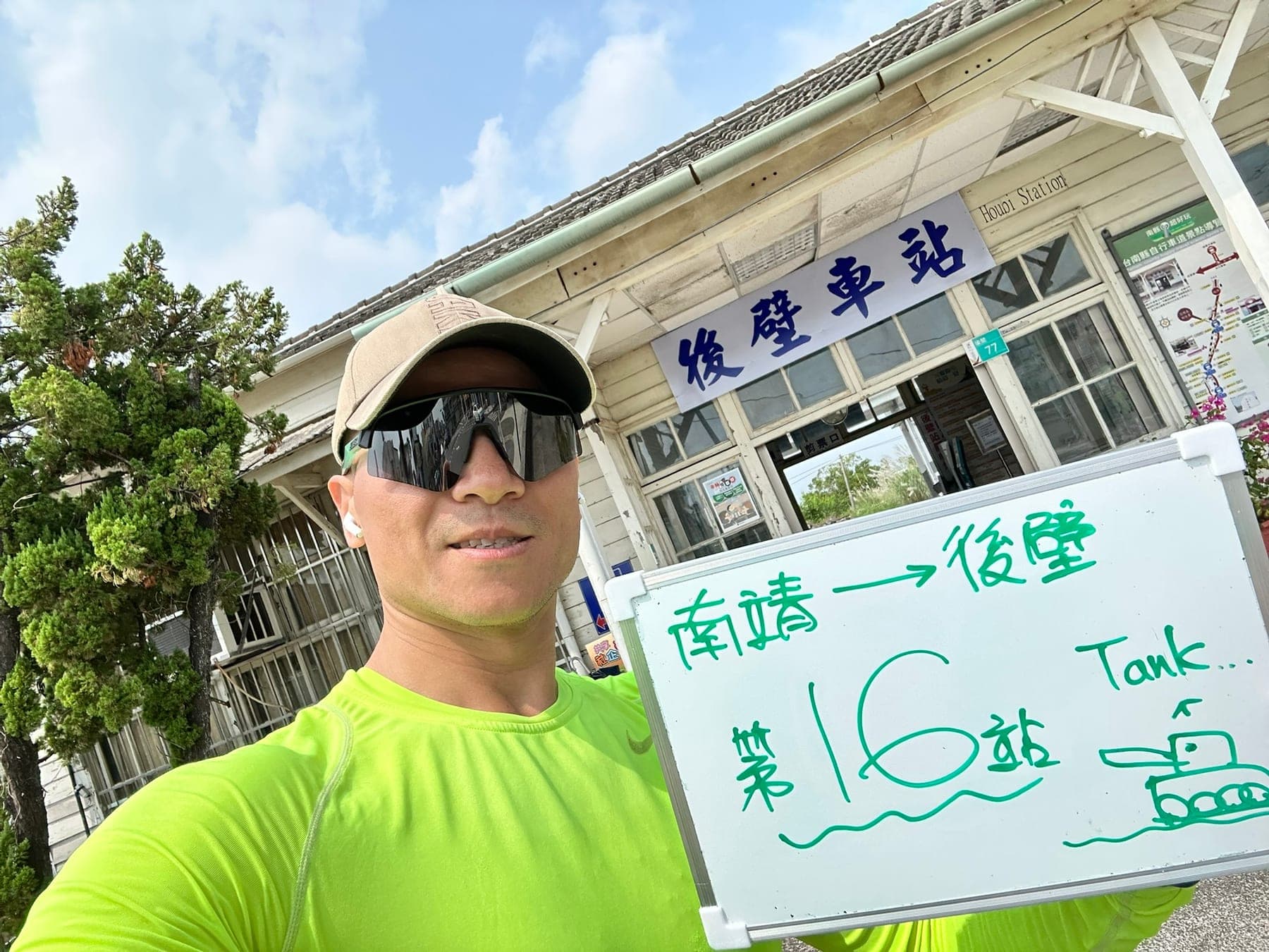 站主在後壁站站牌前的走訪紀錄照,手持寫著「徒步環島 第 16 站 南靖 → 後壁」的白板