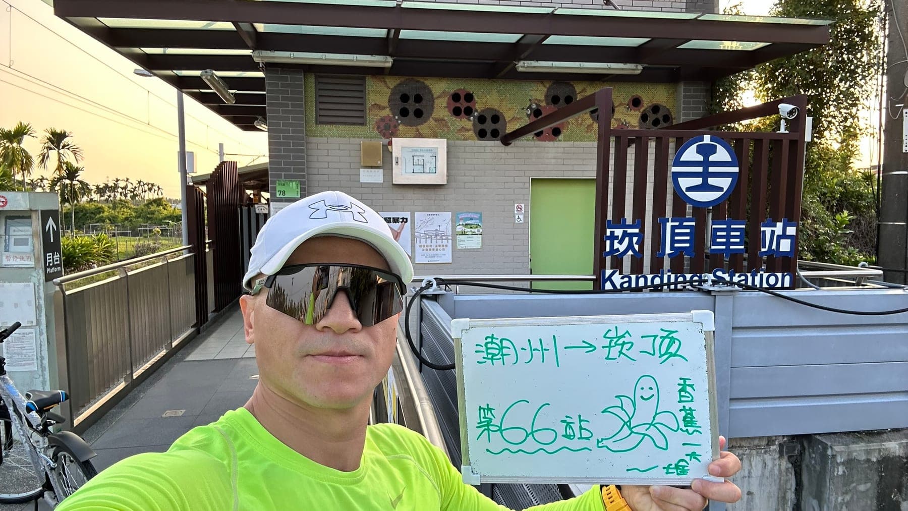 站主在崁頂站站牌前的走訪紀錄照,手持寫著「徒步環島 第 66 站 潮州 → 崁頂」的白板