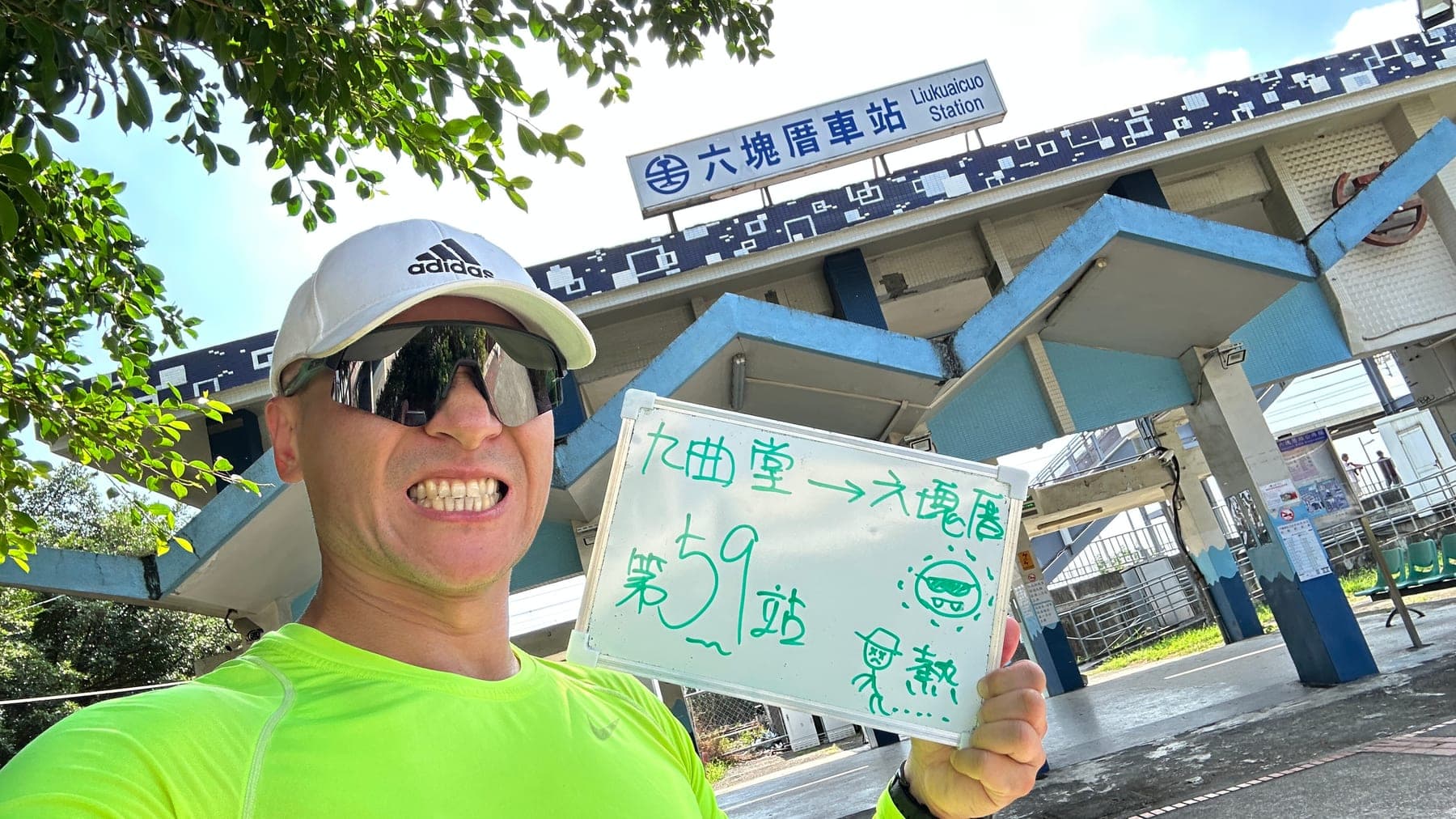 站主在六塊厝站站牌前的走訪紀錄照,手持寫著「徒步環島 第 59 站 九曲堂 → 六塊厝」的白板