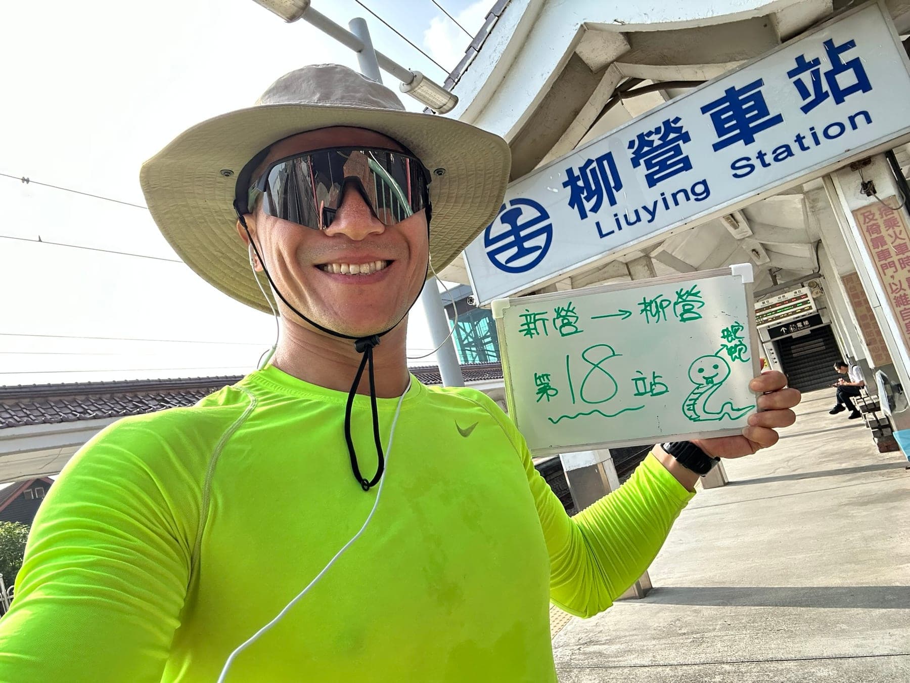 站主在柳營站站牌前的走訪紀錄照,手持寫著「徒步環島 第 18 站 新營 → 柳營」的白板