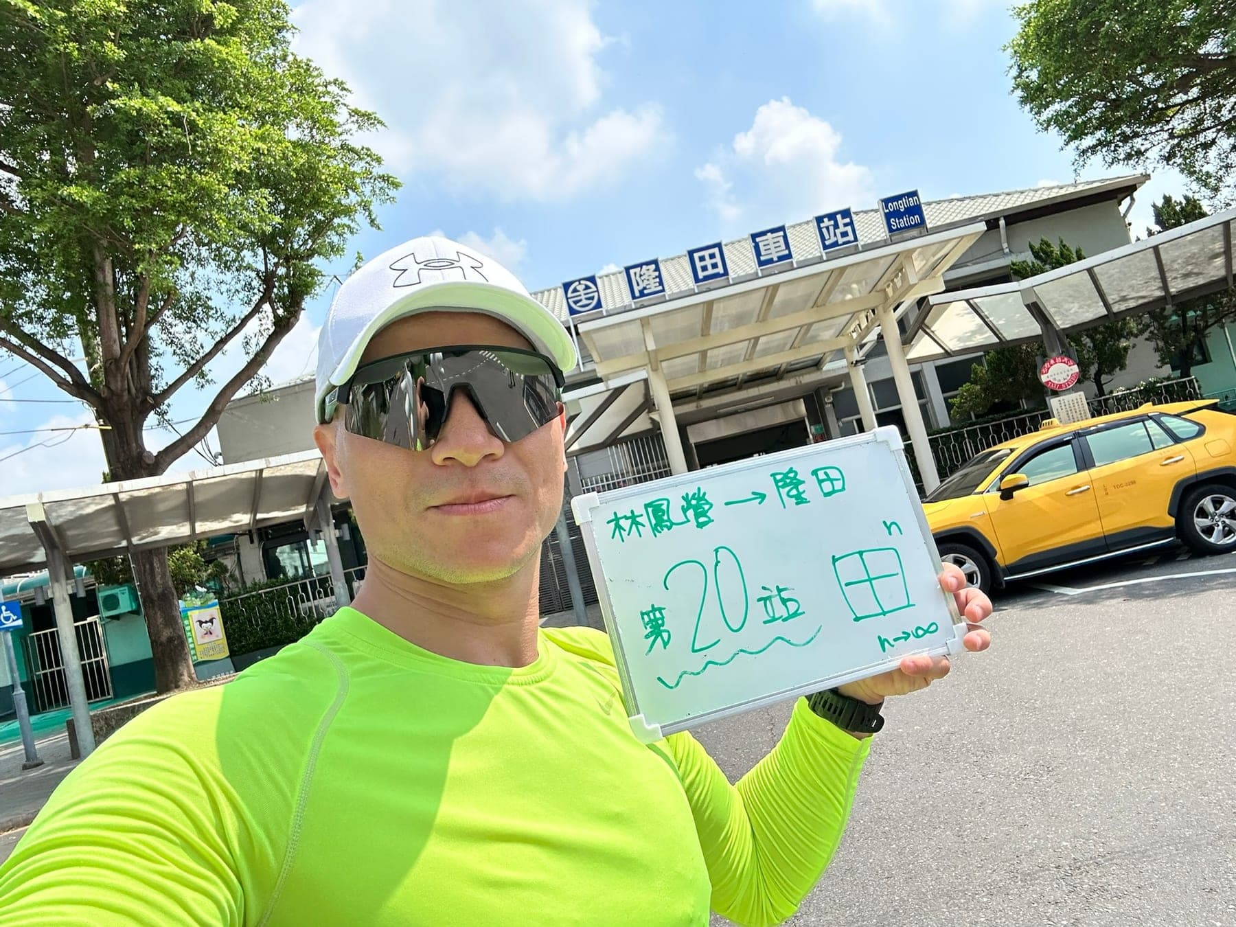 站主在隆田站站牌前的走訪紀錄照,手持寫著「徒步環島 第 20 站 林鳳營 → 隆田」的白板