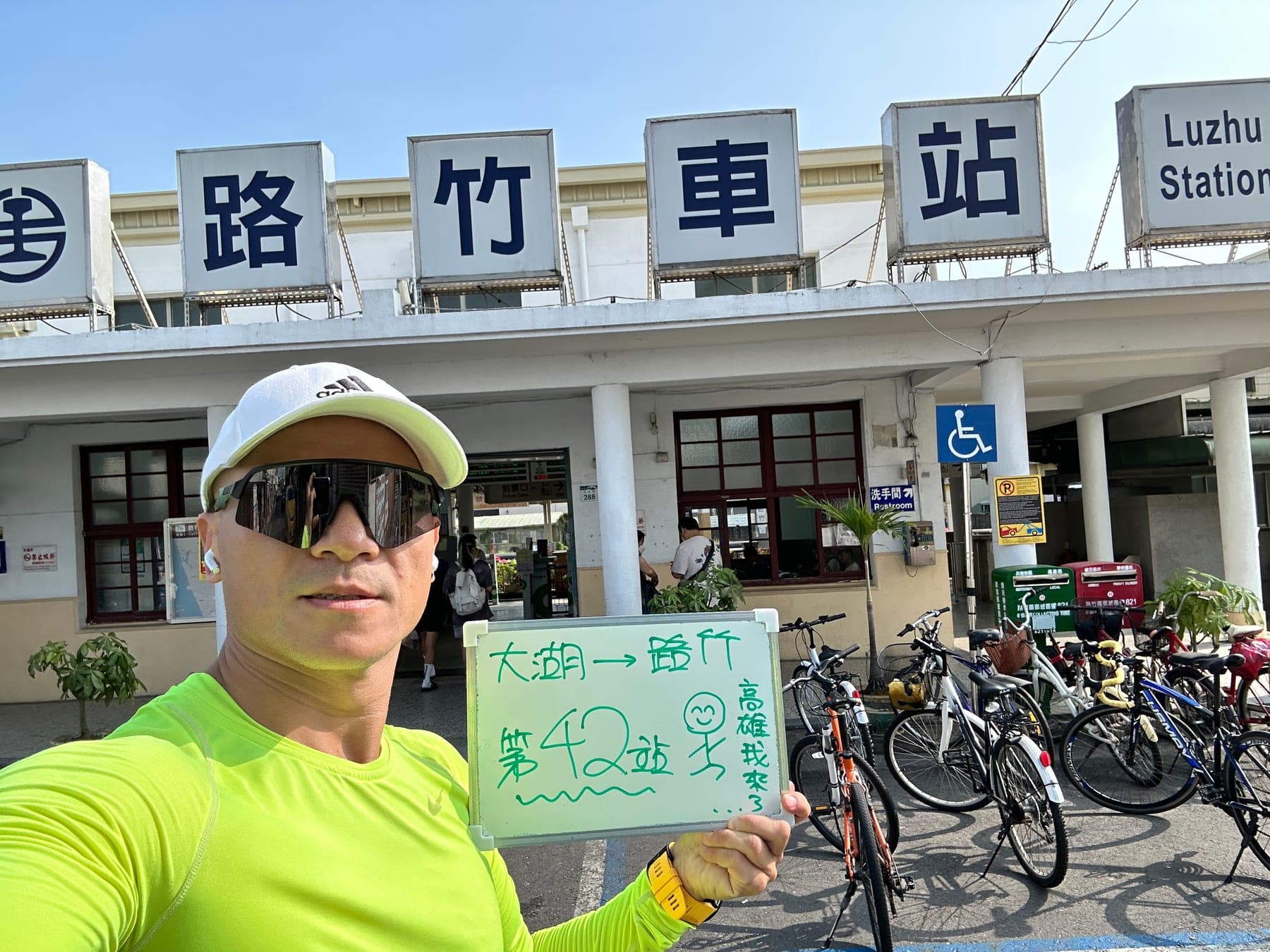 站主在路竹站站牌前的走訪紀錄照,手持寫著「徒步環島 第 42 站 大湖 → 路竹」的白板
