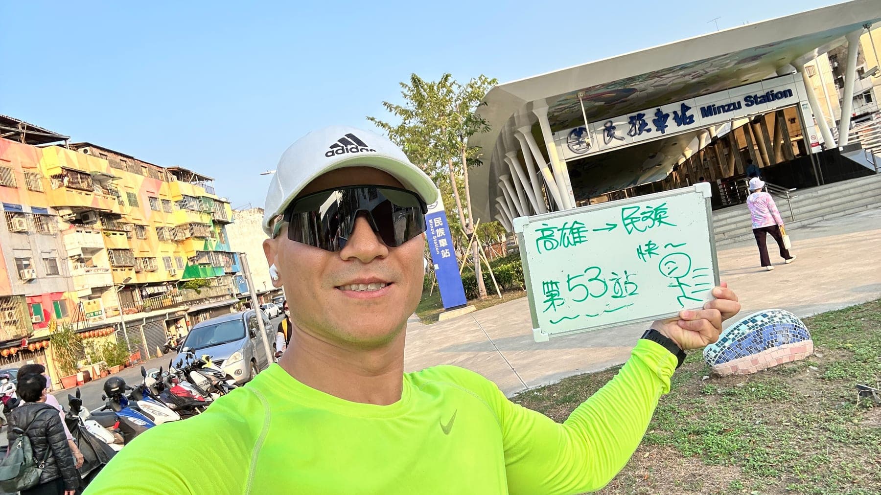 站主在民族站站牌前的走訪紀錄照,手持寫著「徒步環島 第 53 站 高雄 → 民族」的白板