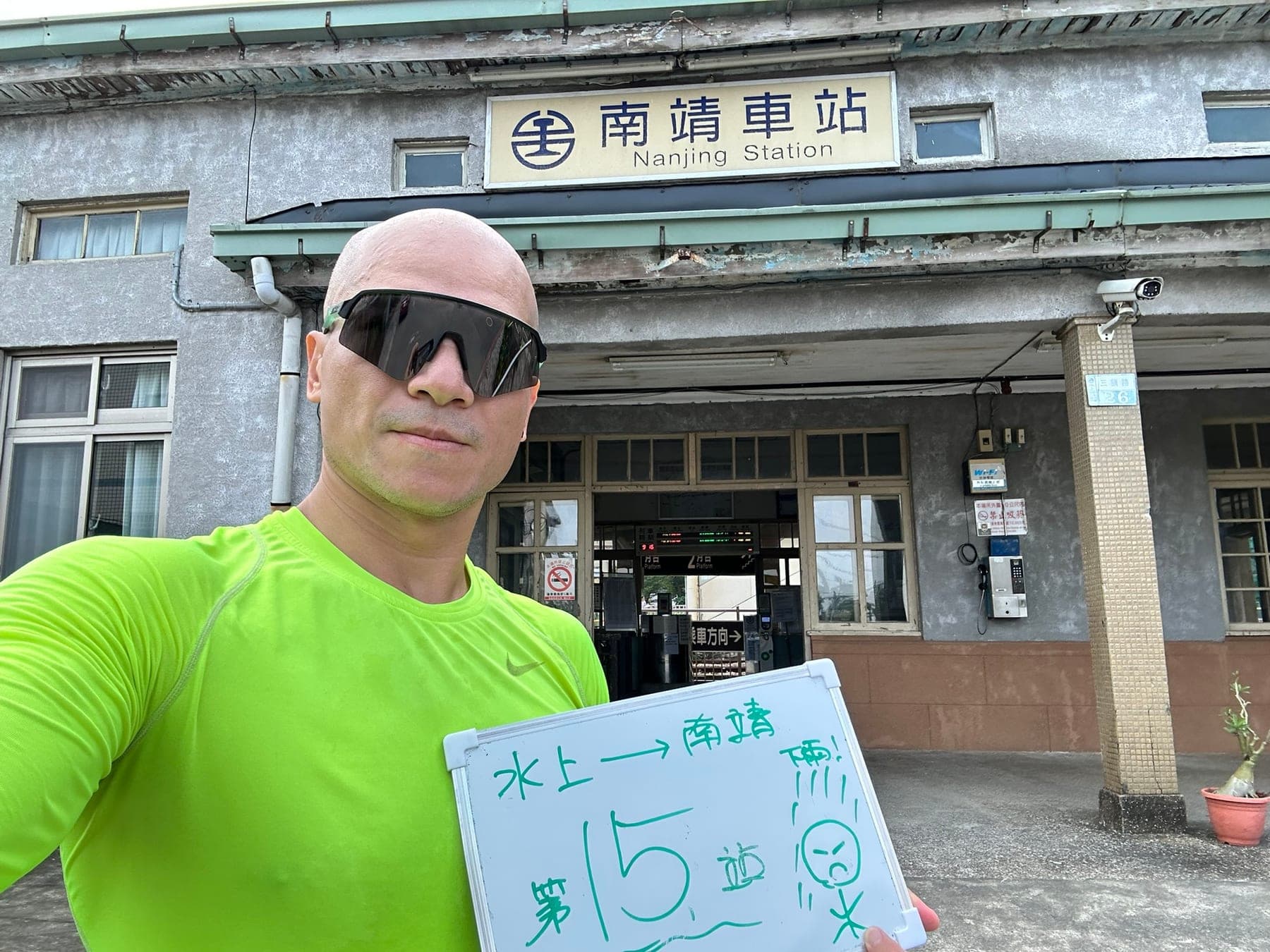 站主在南靖站站牌前的走訪紀錄照,手持寫著「徒步環島 第 15 站 水上 → 南靖」的白板