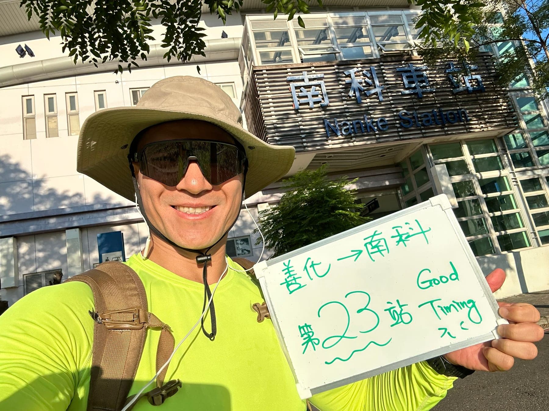 站主在南科站站牌前的走訪紀錄照,手持寫著「徒步環島 第 23 站 善化 → 南科」的白板