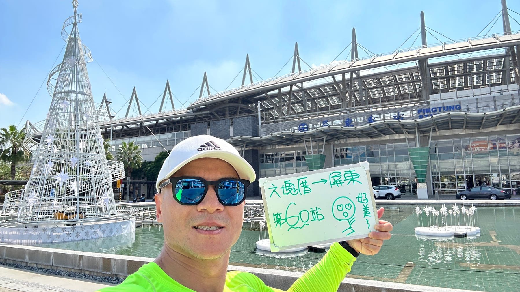 站主在屏東站站牌前的走訪紀錄照,手持寫著「徒步環島 第 60 站 六塊厝 → 屏東」的白板