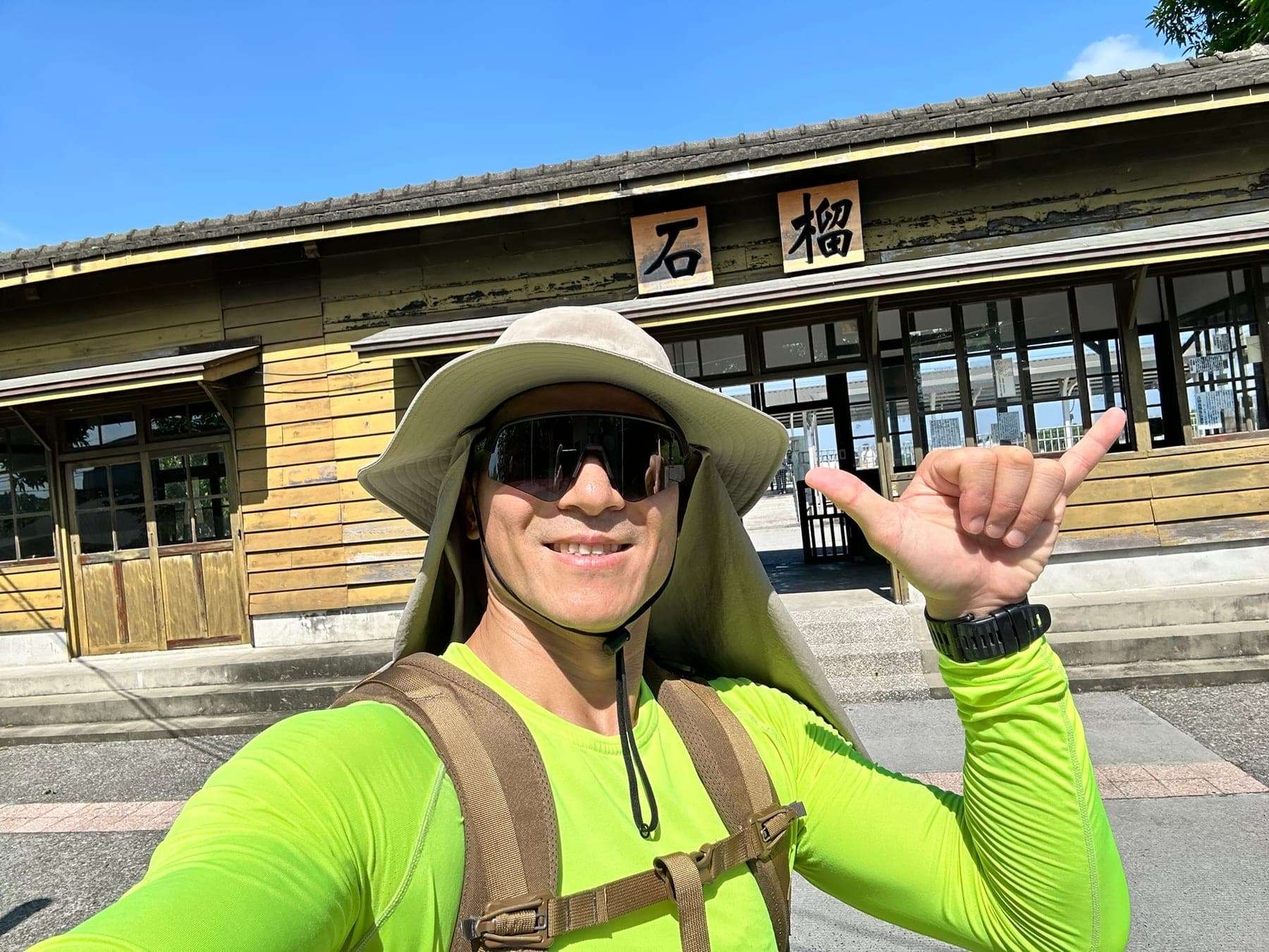 站主在石榴車站前的走訪紀錄照,手比中文的六代表第 6 站,身後是木造站房