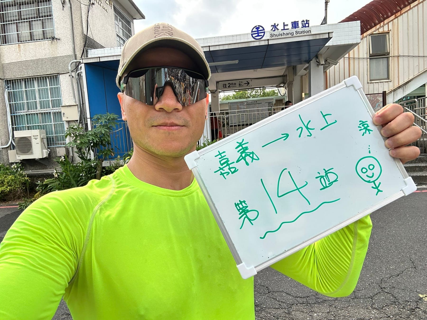 站主在水上站站牌前的走訪紀錄照,手持寫著「徒步環島 第 14 站 嘉義 → 水上」的白板
