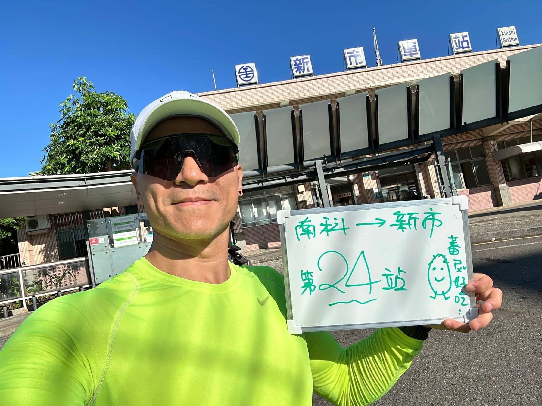 站主在新市站站牌前的走訪紀錄照,手持寫著「徒步環島 第 24 站 南科 → 新市」的白板