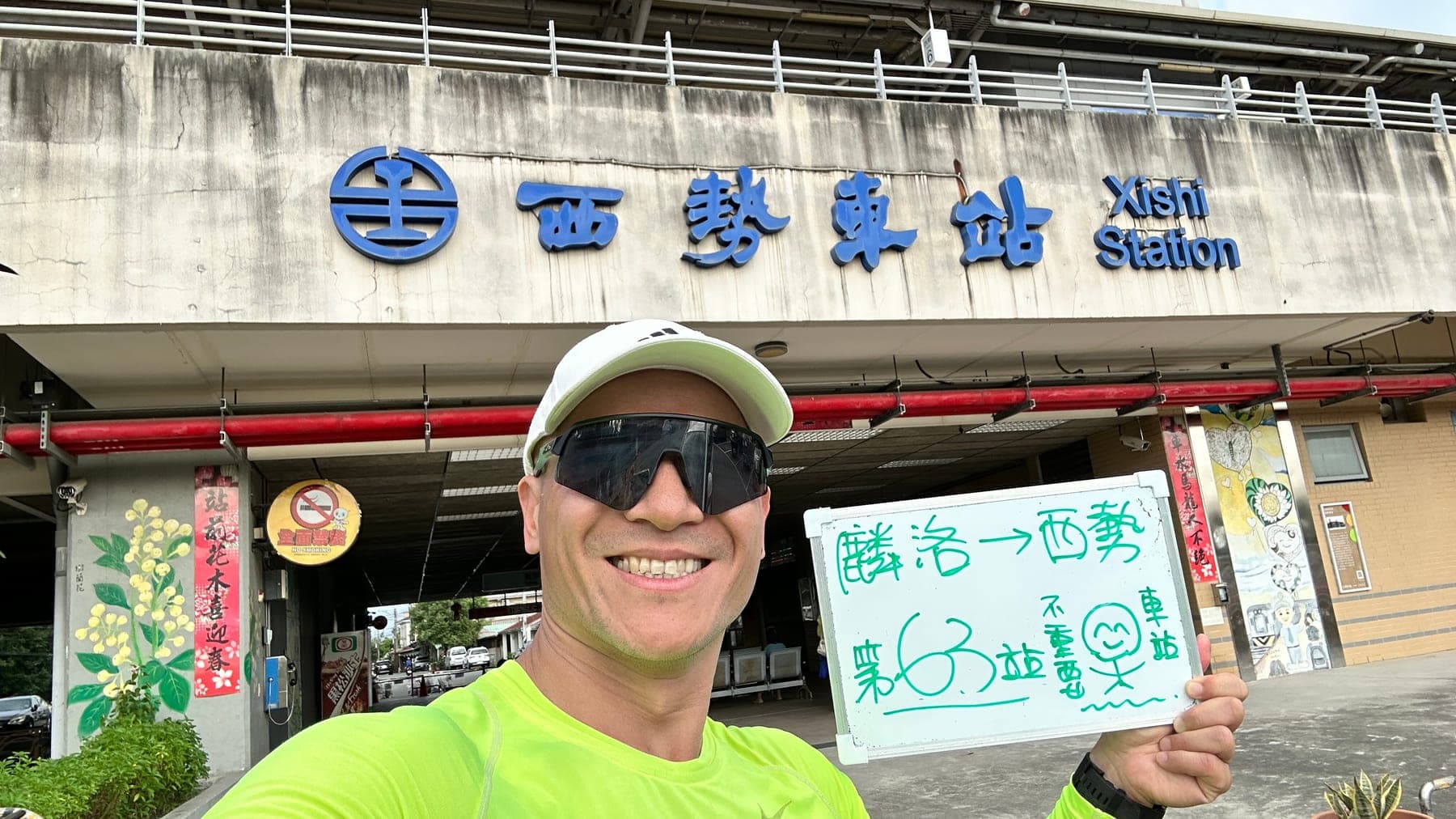 站主在西勢站站牌前的走訪紀錄照,手持寫著「徒步環島 第 63 站 麟洛 → 西勢」的白板