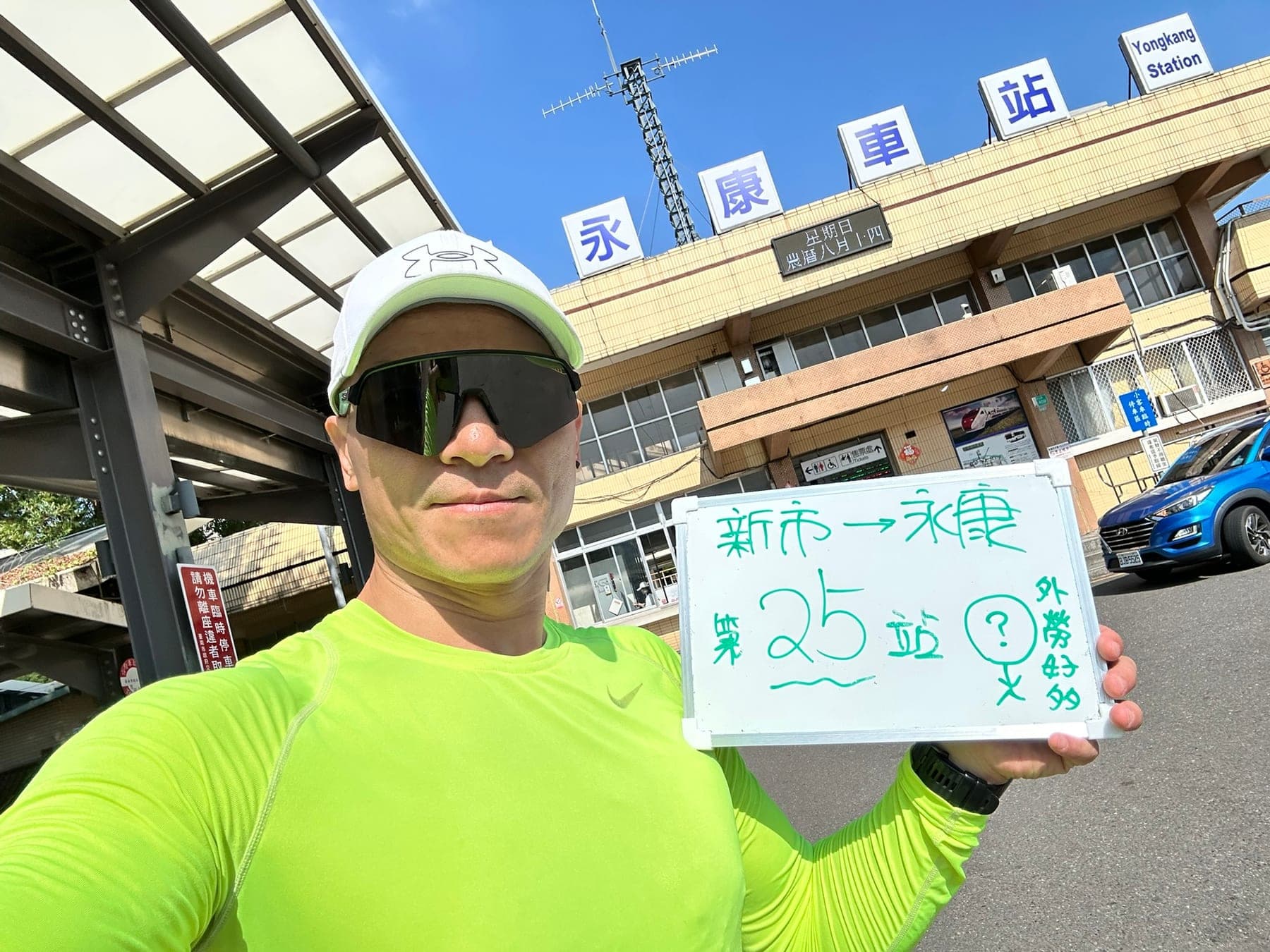 站主在永康站站牌前的走訪紀錄照,手持寫著「徒步環島 第 25 站 新市 → 永康」的白板