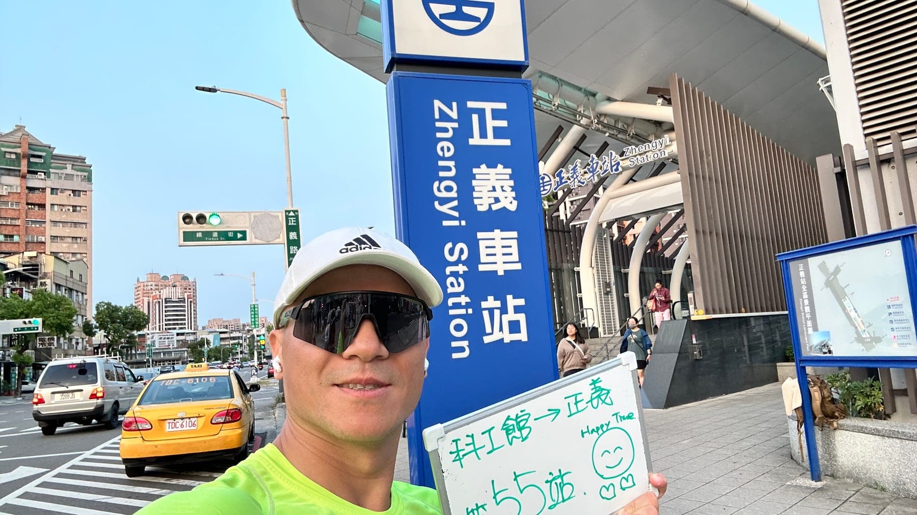 站主在正義站站牌前的走訪紀錄照,手持寫著「徒步環島 第 55 站 科工館 → 正義」的白板