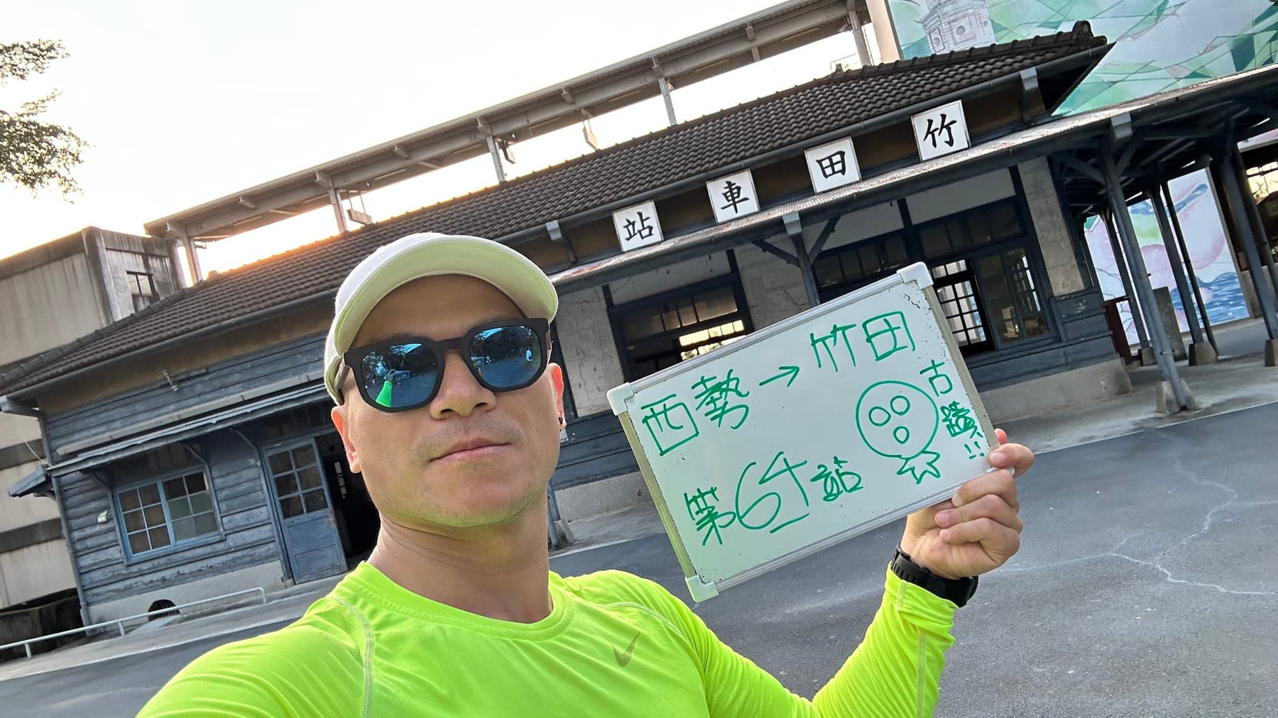 站主在竹田站站牌前的走訪紀錄照,手持寫著「徒步環島 第 64 站 西勢 → 竹田」的白板
